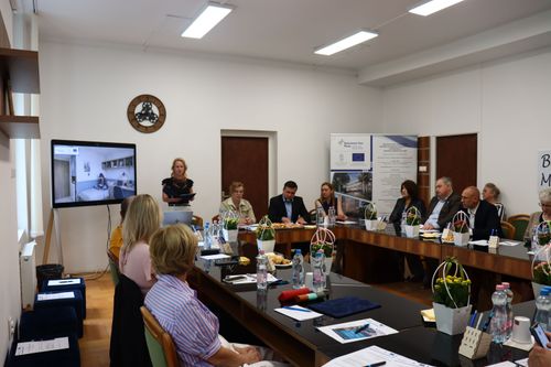 Tárgyalóterem körben ülő résztvevőkkel, kivetítéssel